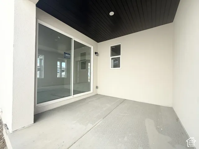Covered patio with a concrete surface, white stucco exterior, and a dark wood-finish ceiling