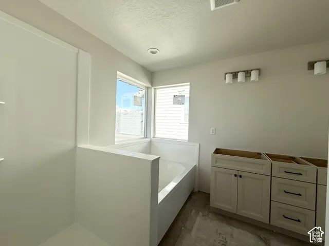 Recessed ceiling lighting, corner windows, built-in tub, separate shower enclosure, and vanity cabinetry with dark hardware