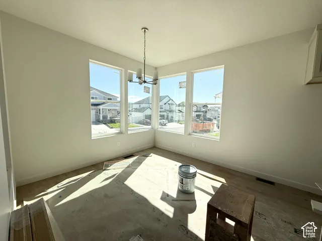 Expansive windows with white trim, contemporary chandelier, light-colored walls, and unfinished flooring