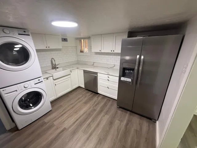 White shaker cabinetry with stone-finish countertops, subway tile backsplash, stainless steel refrigerator, and wood-finish flooring