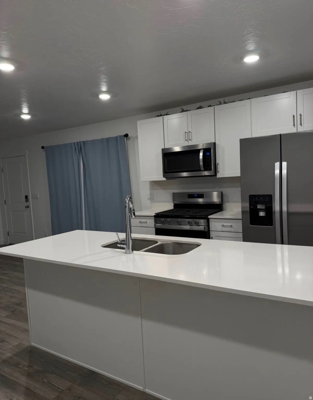 Kitchen featuring white cabinetry, stainless steel appliances, a center island with sink, and light-toned countertops