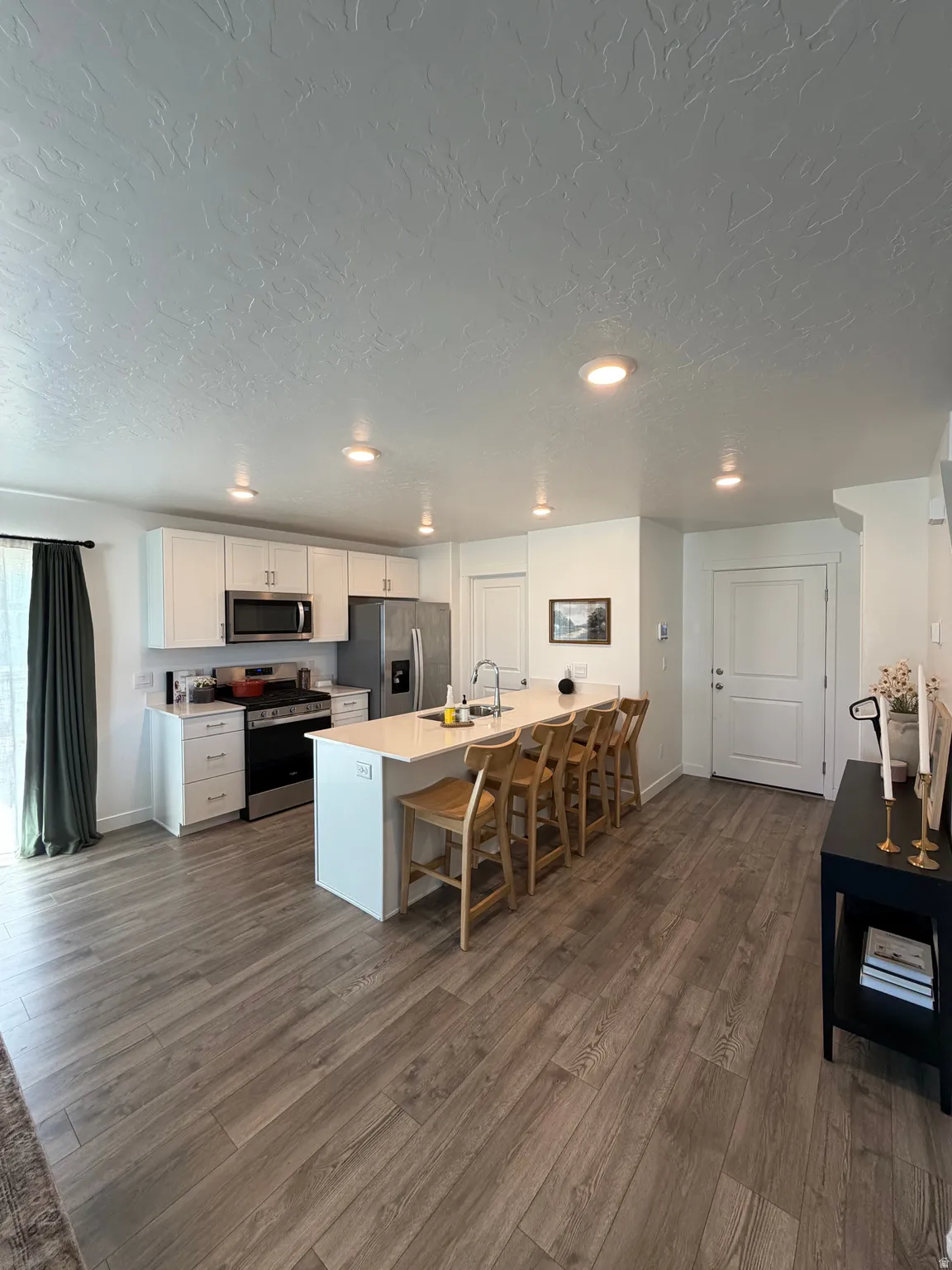 Open-concept kitchen with white cabinetry and an integrated island, stainless steel appliances, wood-finish flooring, and recessed lighting