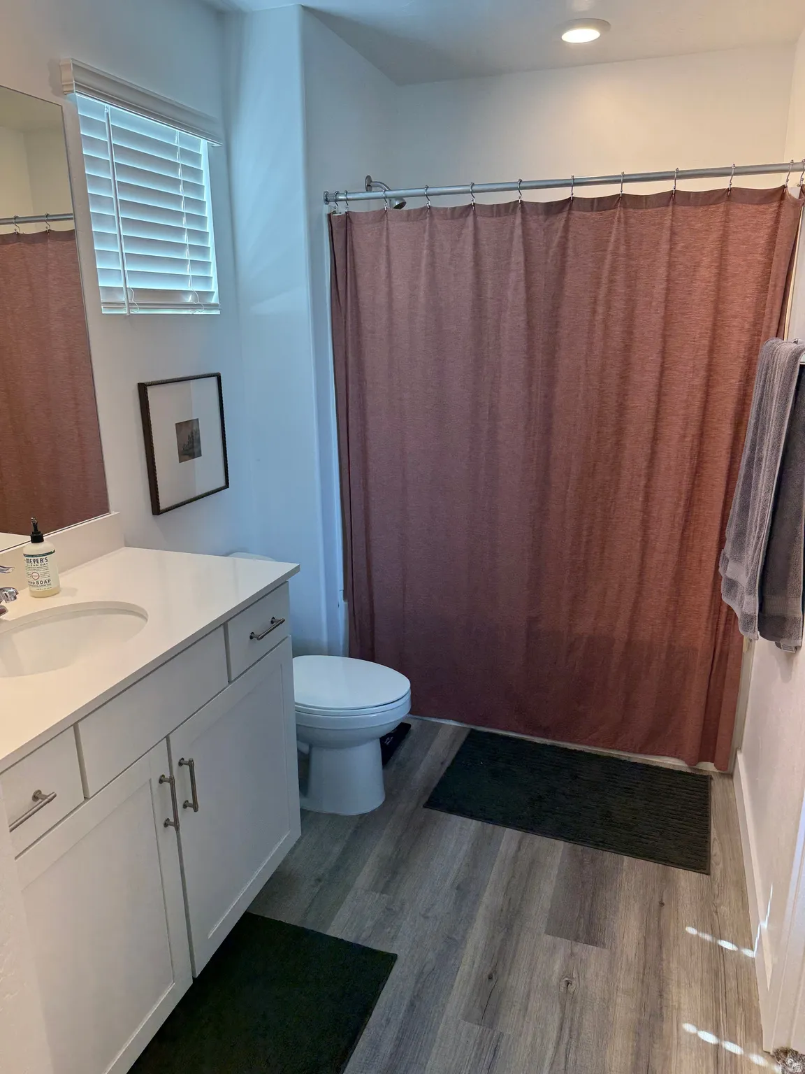 White vanity with a single basin sink and brushed nickel hardware, wood-finish flooring, recessed lighting, and a window with blinds