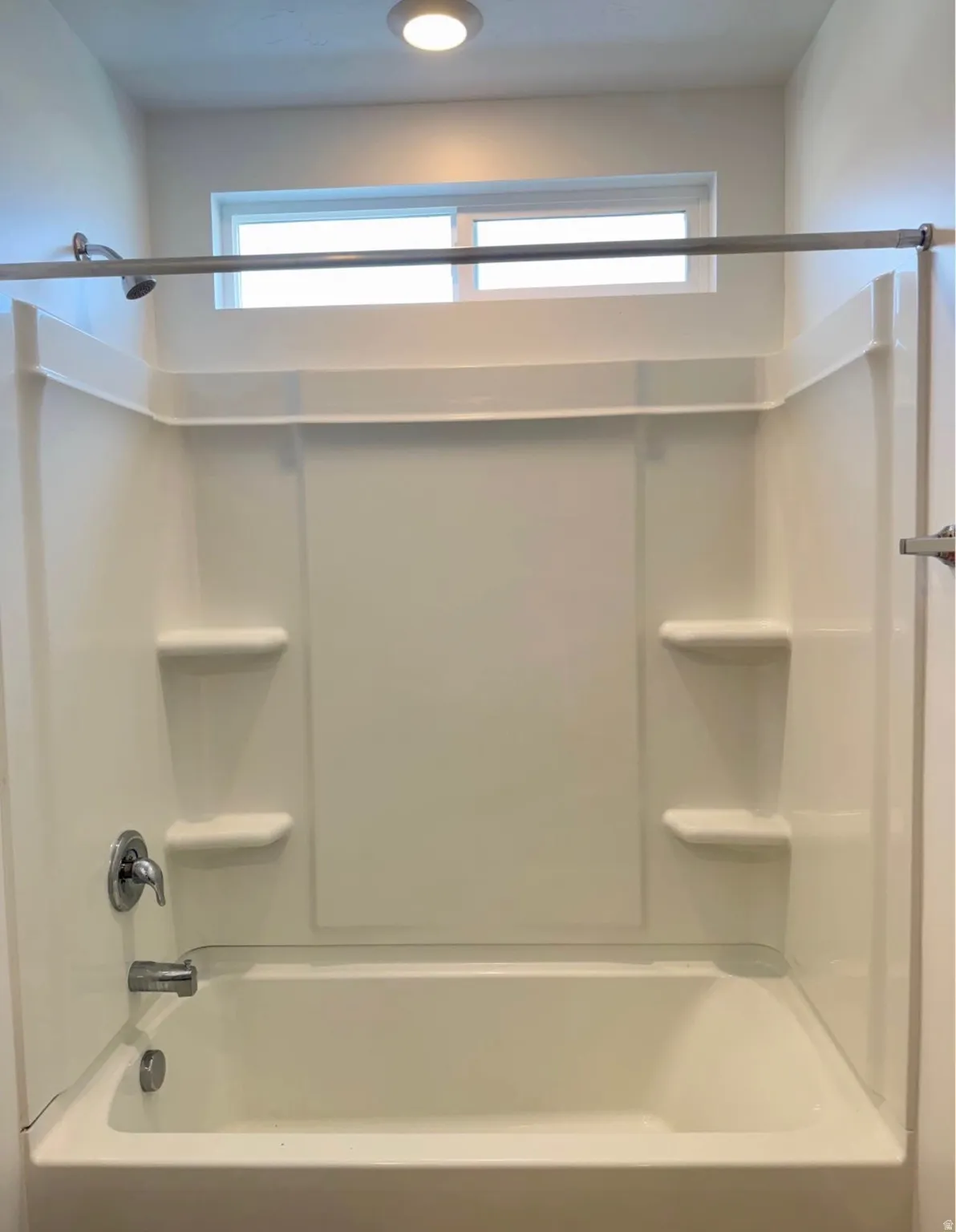 Bathtub with integrated shower surround, built-in shelving, and a horizontal window