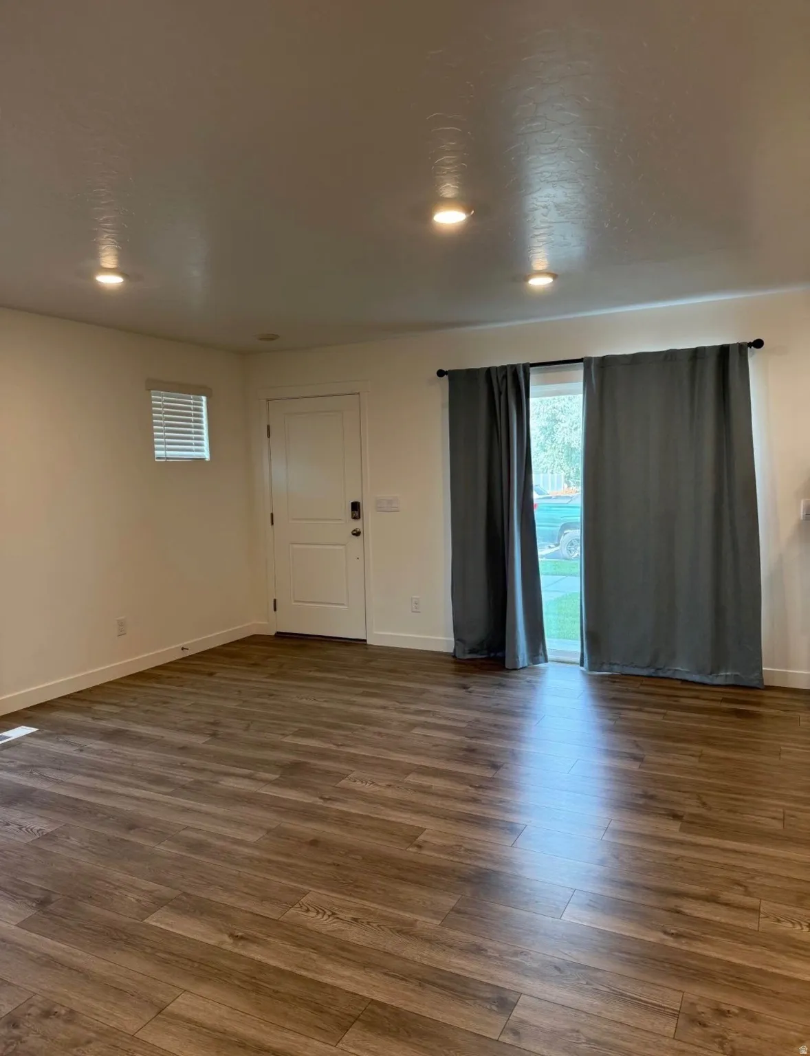 Wood-finish flooring, recessed ceiling lighting, a contemporary white door, and a sliding glass door