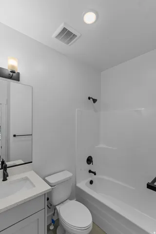 Bathroom featuring a white bathtub with dark fixtures, a white toilet, and a vanity with a light-colored countertop