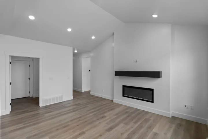 Vaulted ceiling, recessed lighting, wood-finish flooring, linear electric fireplace, and a floating mantel