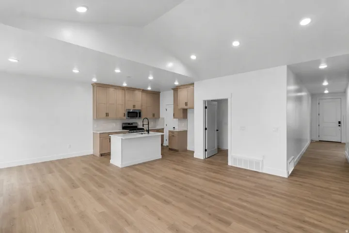 Open-concept space featuring wood-finish flooring, recessed lighting, and a kitchen island with a black gooseneck faucet