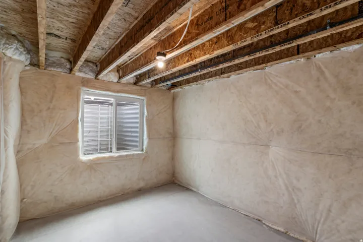 Unfinished interior space with exposed ceiling joists, concrete flooring, and a single-pane window with a metal grate
