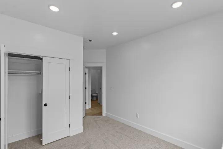 Recessed ceiling lighting, carpeted flooring, white interior doors, and a built-in closet with hanging rod