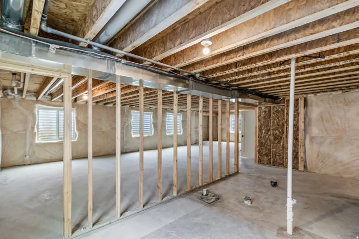 Unfinished basement with exposed wood framing, concrete flooring, multiple windows, and exposed ceiling joists