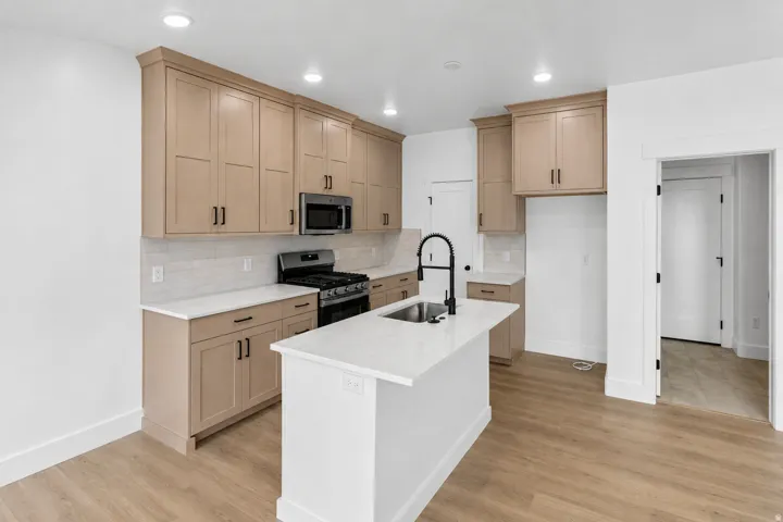 Kitchen featuring wood-finish flooring, recessed lighting, a central island with an undermount sink, light-toned cabinetry, and white countertops