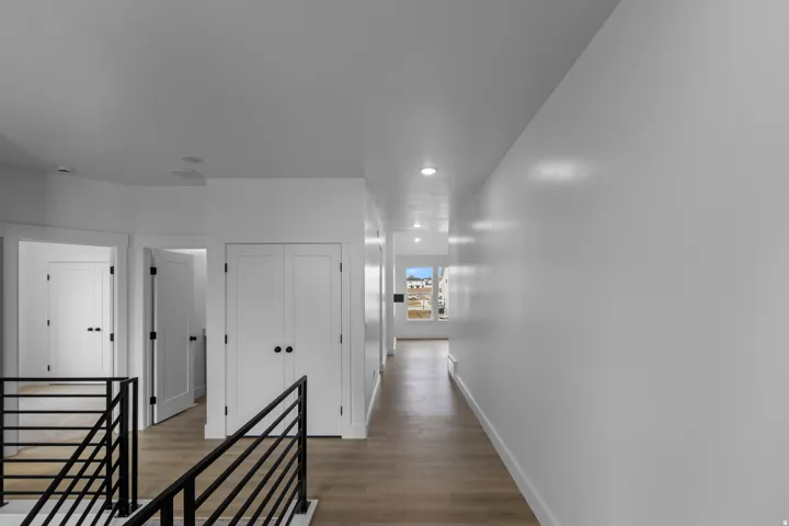 Hallway with wood-finish flooring, recessed lighting, white panel doors, and black metal railings