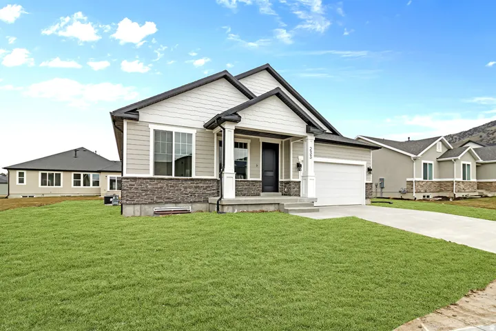 Modern ranch-style exterior with gray siding, stone veneer accents, an attached garage, a covered front porch, and a concrete driveway
