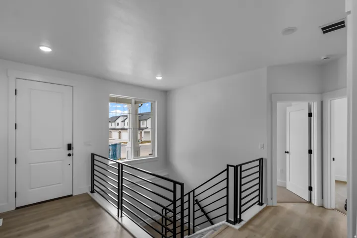 Open upper landing with recessed lighting, modern horizontal metal railings, wood-finish flooring, and white trim