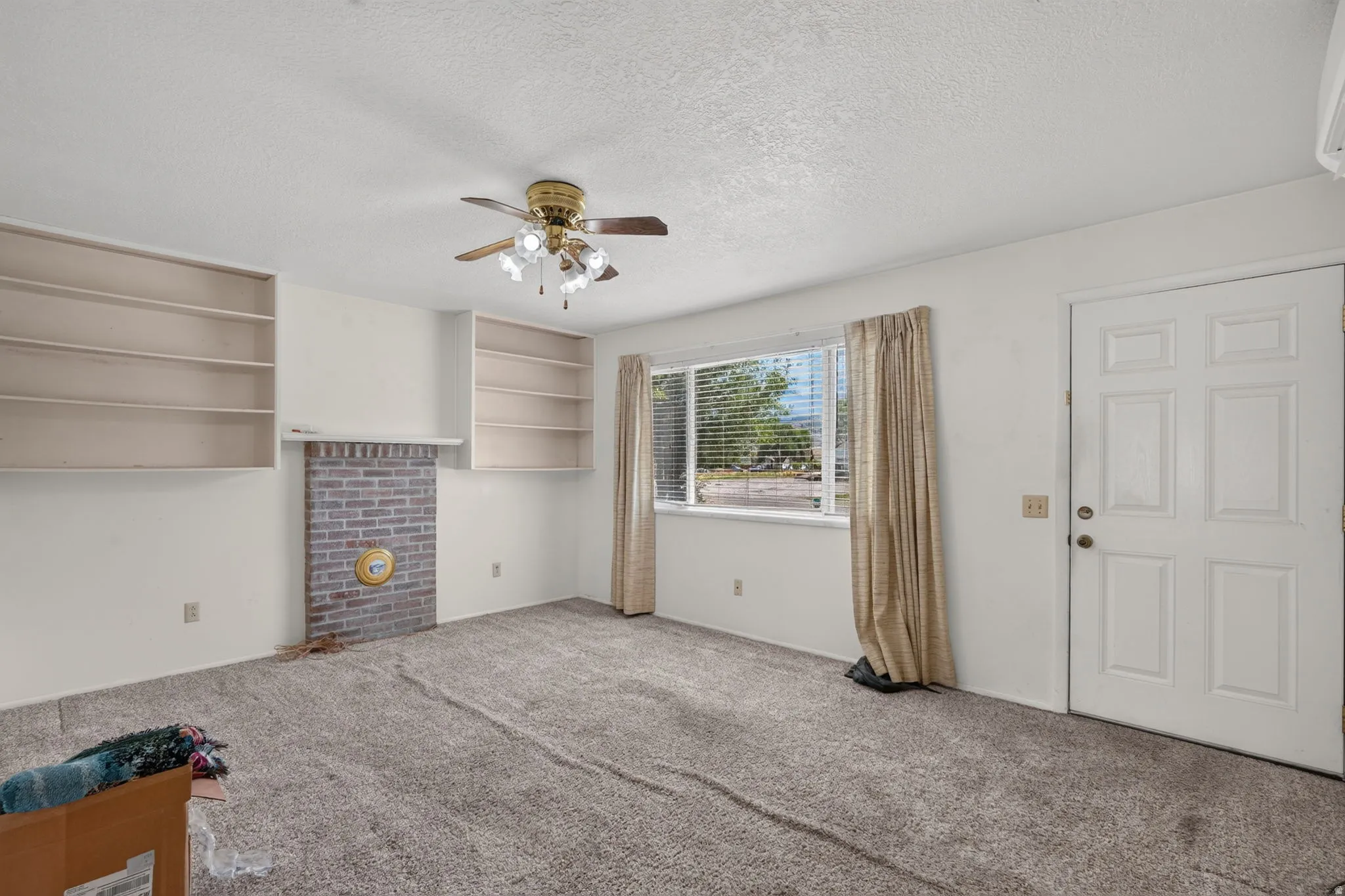 Brick fireplace with a mantel, flanking built-in shelving, ceiling fan with illumination, and a paneled entry door