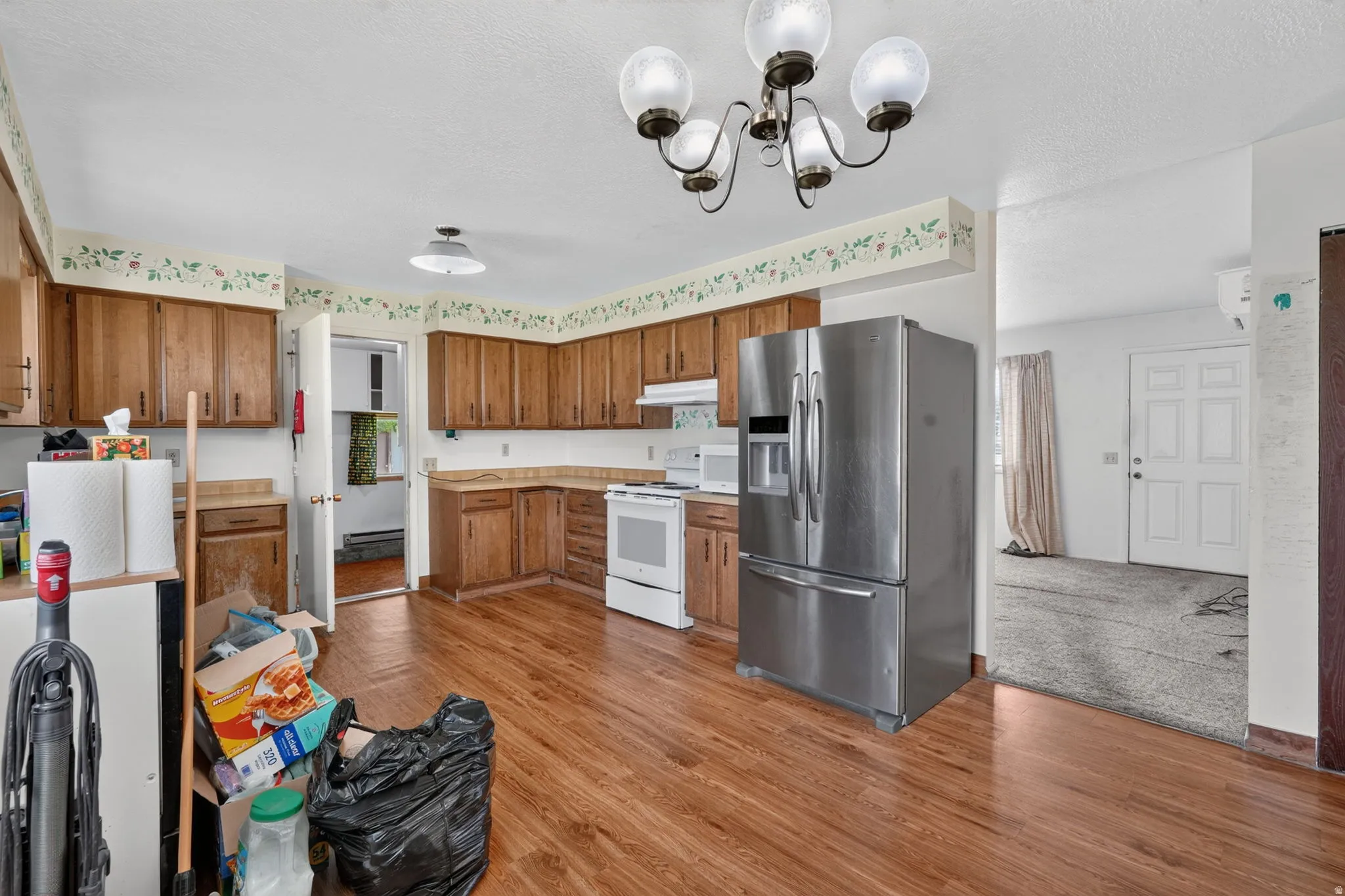 Kitchen featuring wood-finish flooring, wood cabinetry, stainless steel refrigerator, white electric range, and a chandelier light fixture