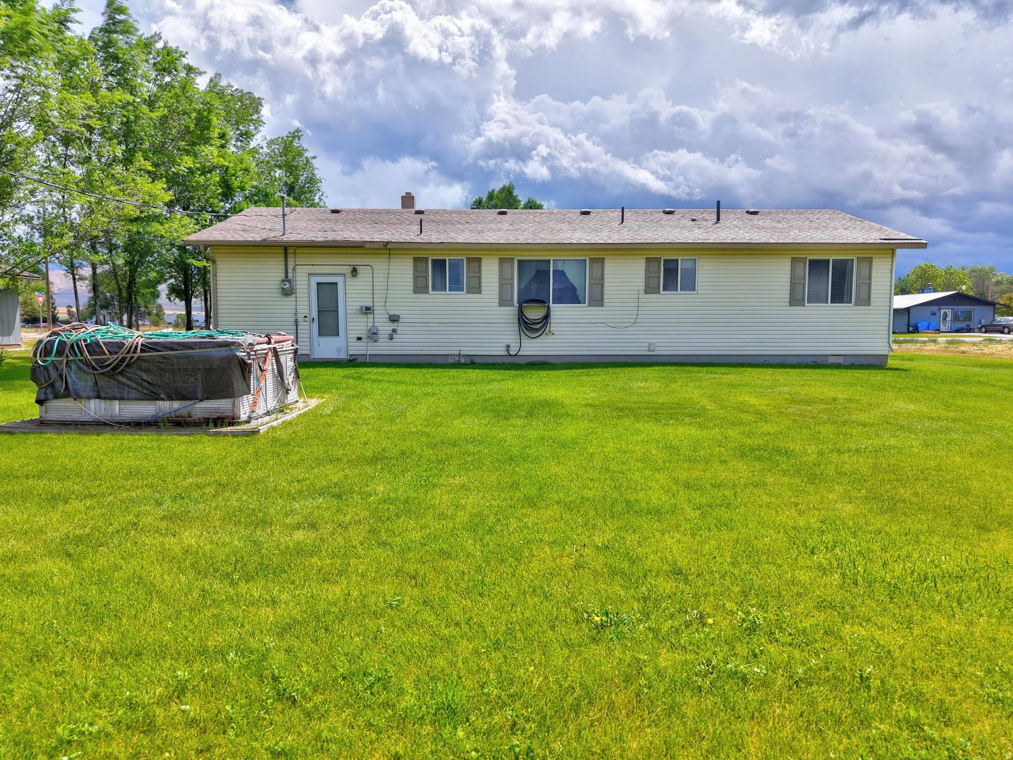 Single-story residence with light-colored siding, multiple windows with shutters, and a well-maintained green lawn