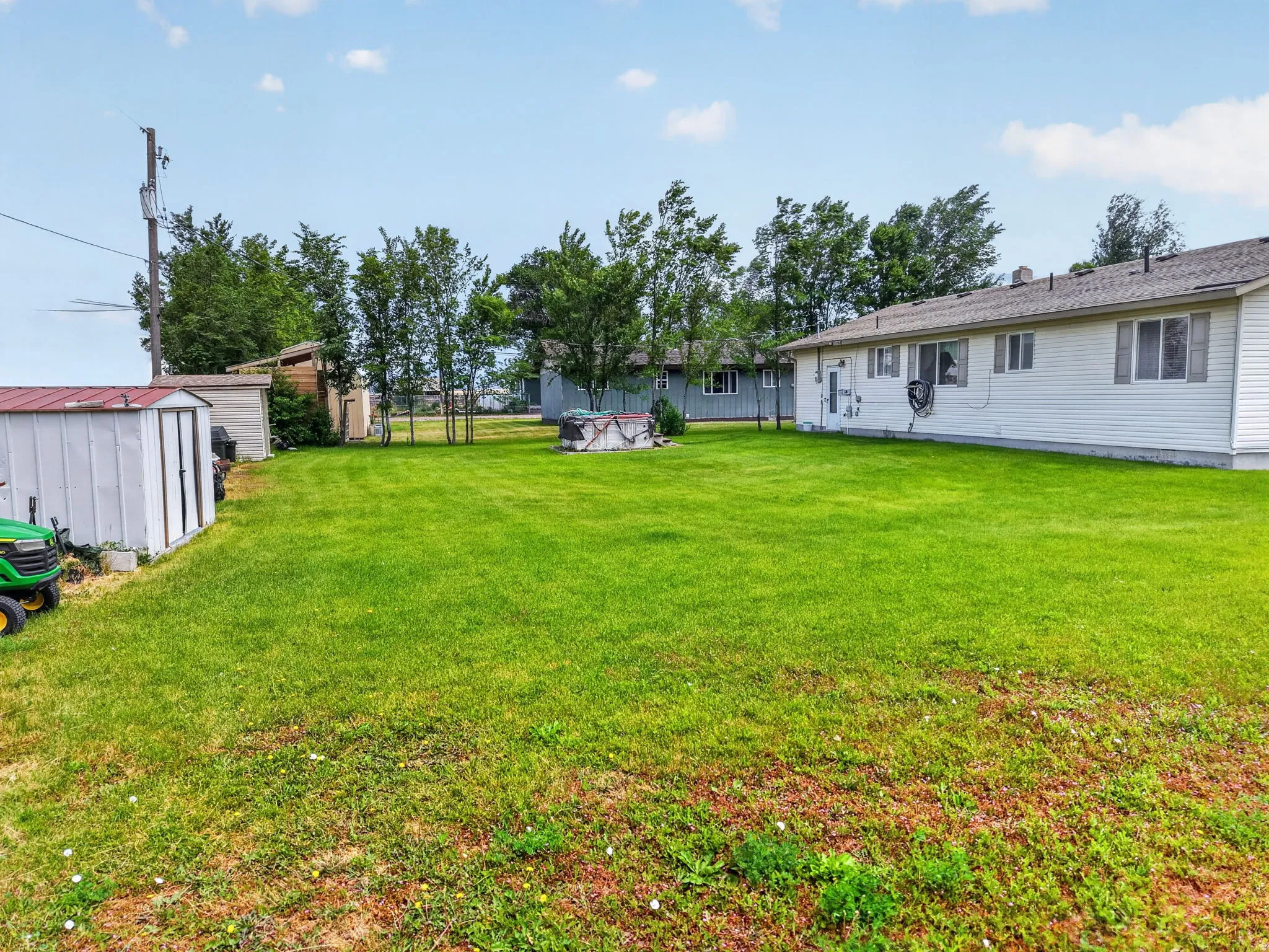 Expansive lawn area with a white storage shed featuring a red metal roof