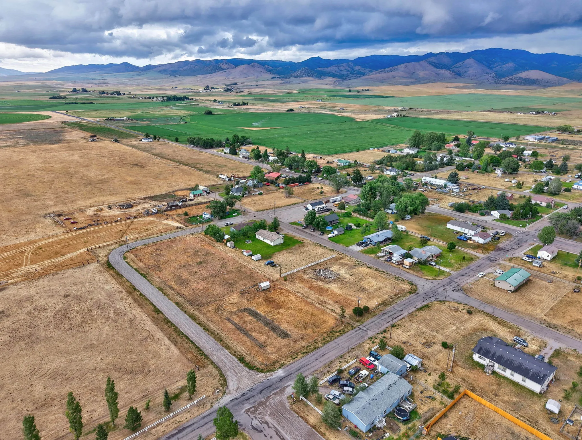 Expansive landscape featuring distant mountains, agricultural fields, and community roads
