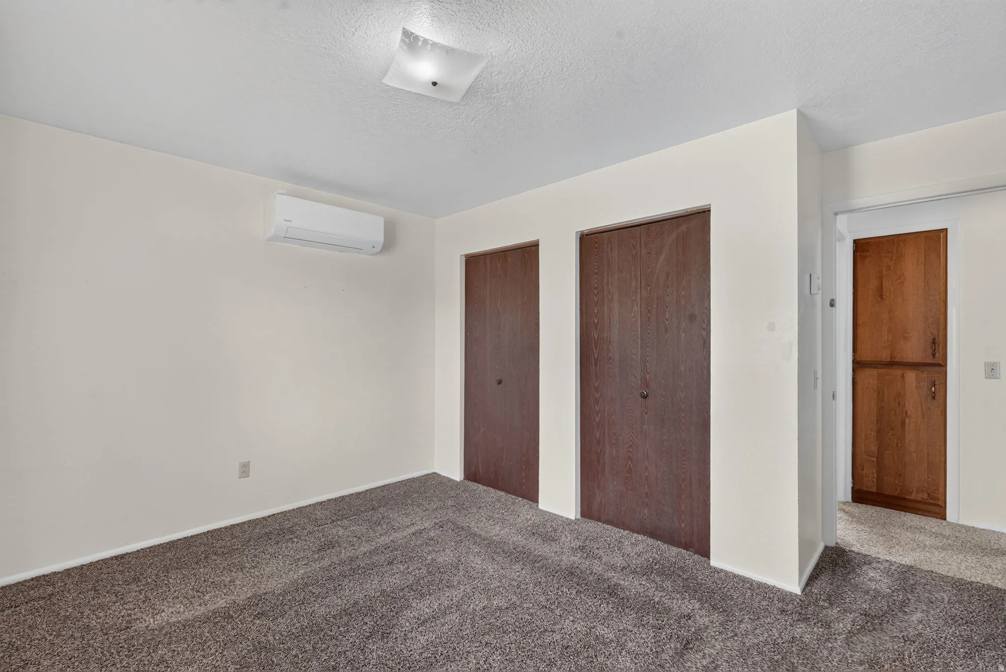 Wall-mounted climate control unit, two dark wood-finish closet doors, light-colored wall paint, and textured carpeting