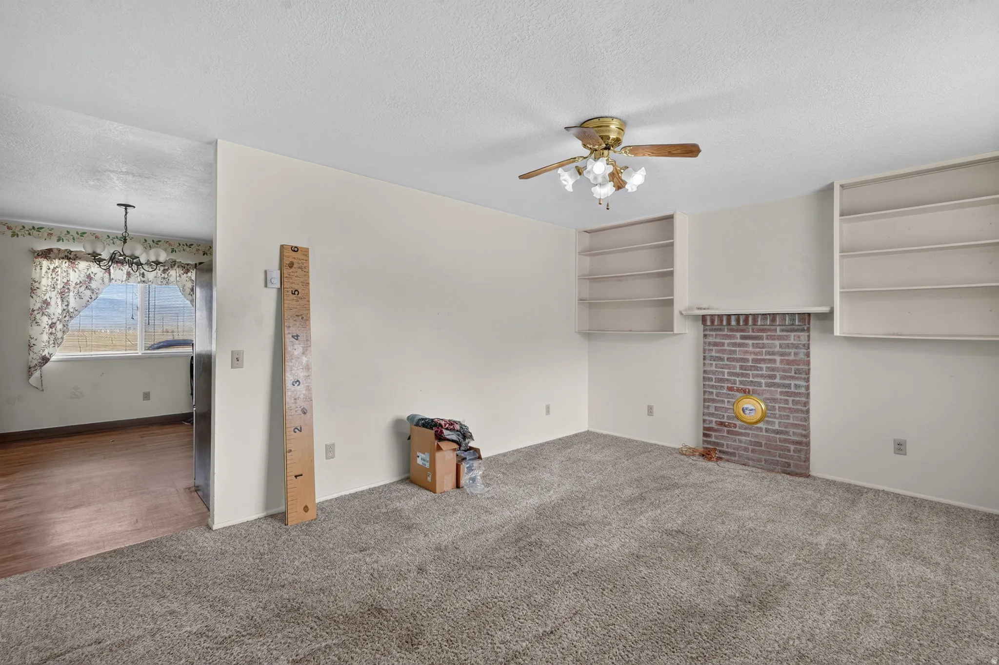 Carpeted living area with a brick fireplace, built-in shelving, and a ceiling fan