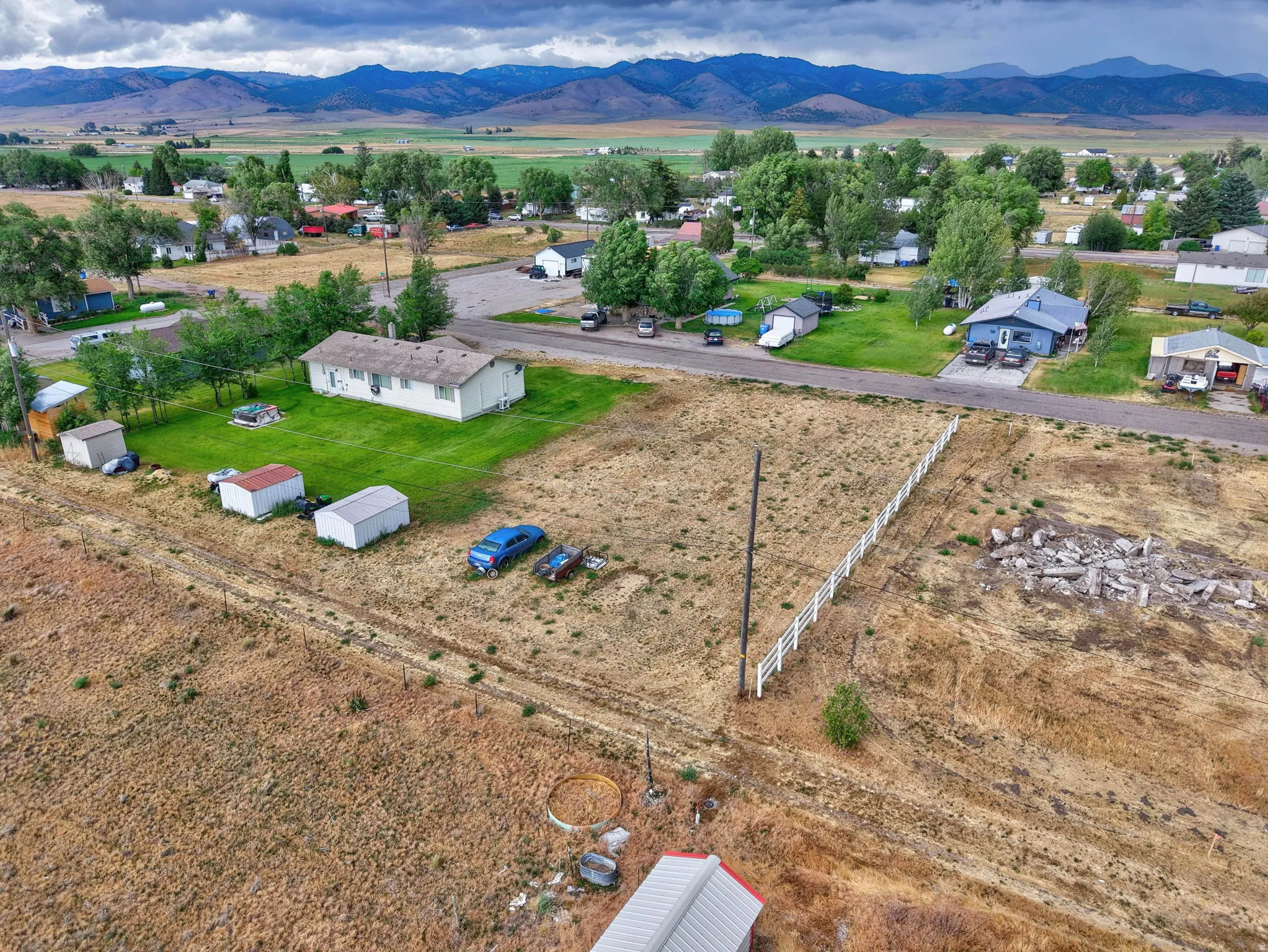Expansive parcel featuring a white fence, scattered outbuildings, and a mountain backdrop