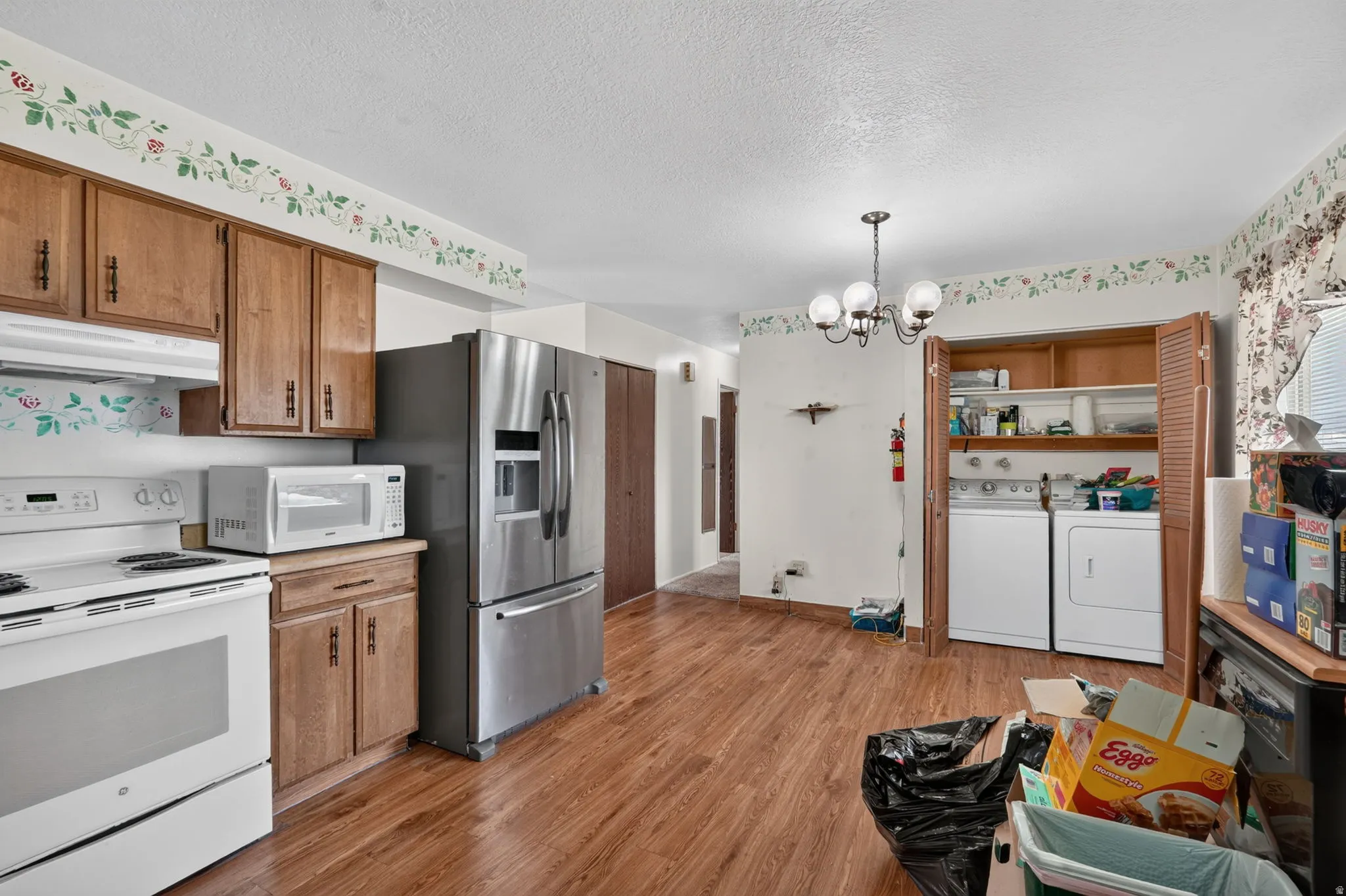 Wood-finish flooring throughout, stainless steel refrigerator, built-in wooden cabinetry, white range, and laundry appliances within a dedicated alcove