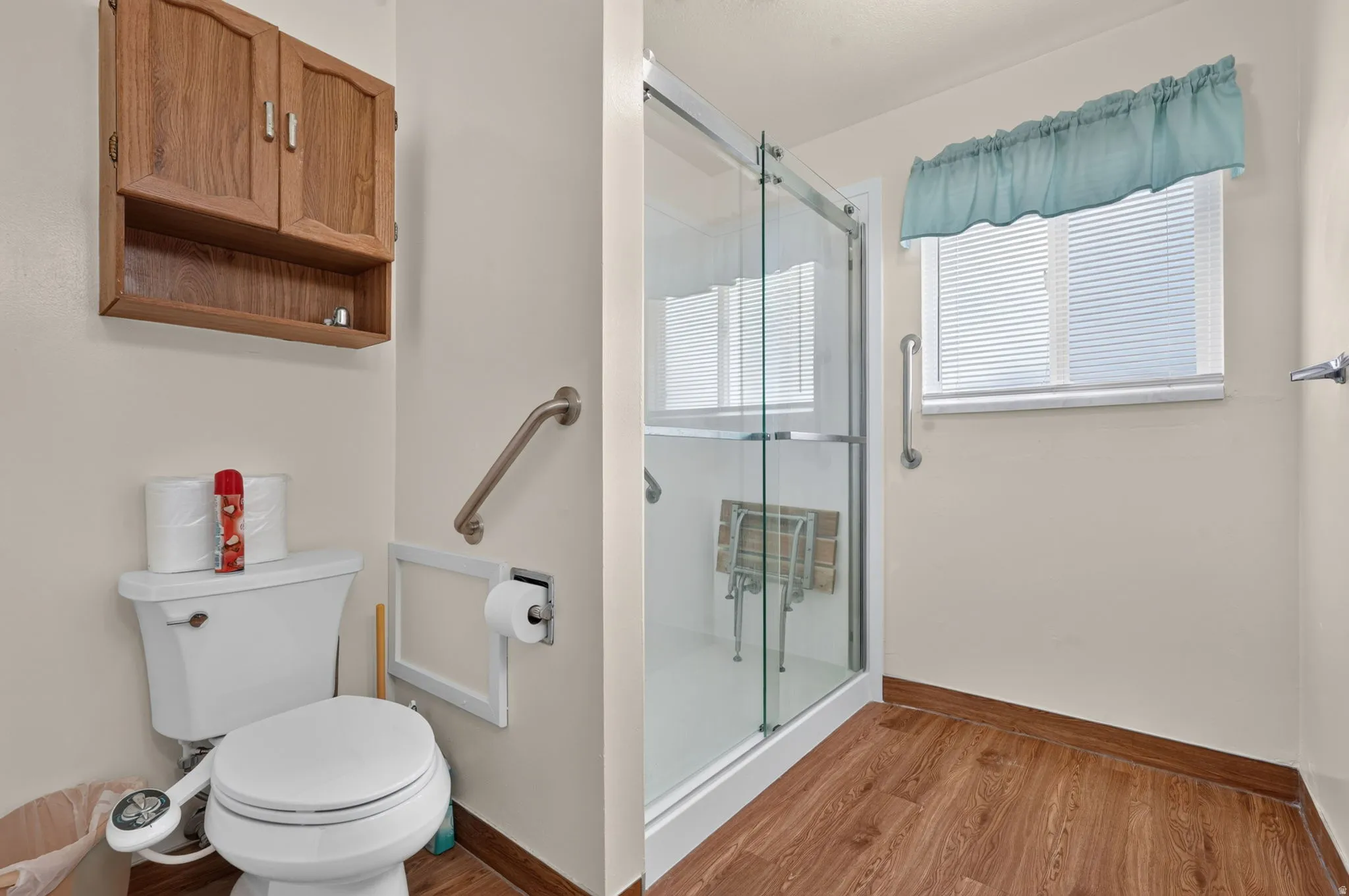 Walk-in shower with clear glass enclosure, wood-finish flooring, and a wall-mounted wooden cabinet