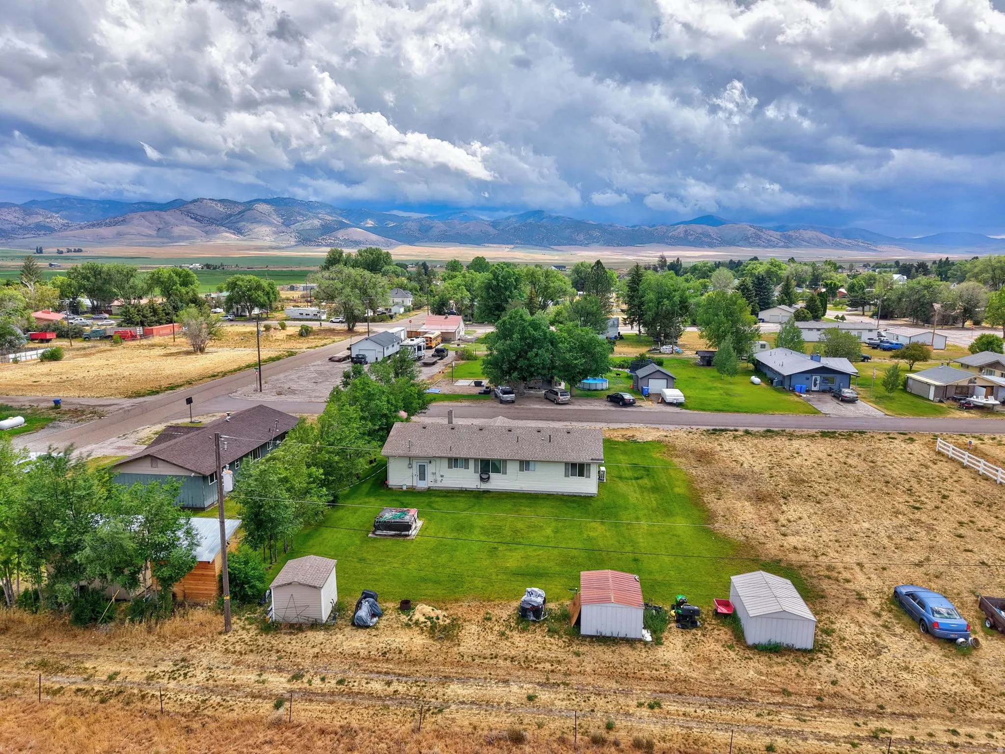 Expansive property featuring a single-story residence, multiple outbuildings, mature trees, and a mountain backdrop