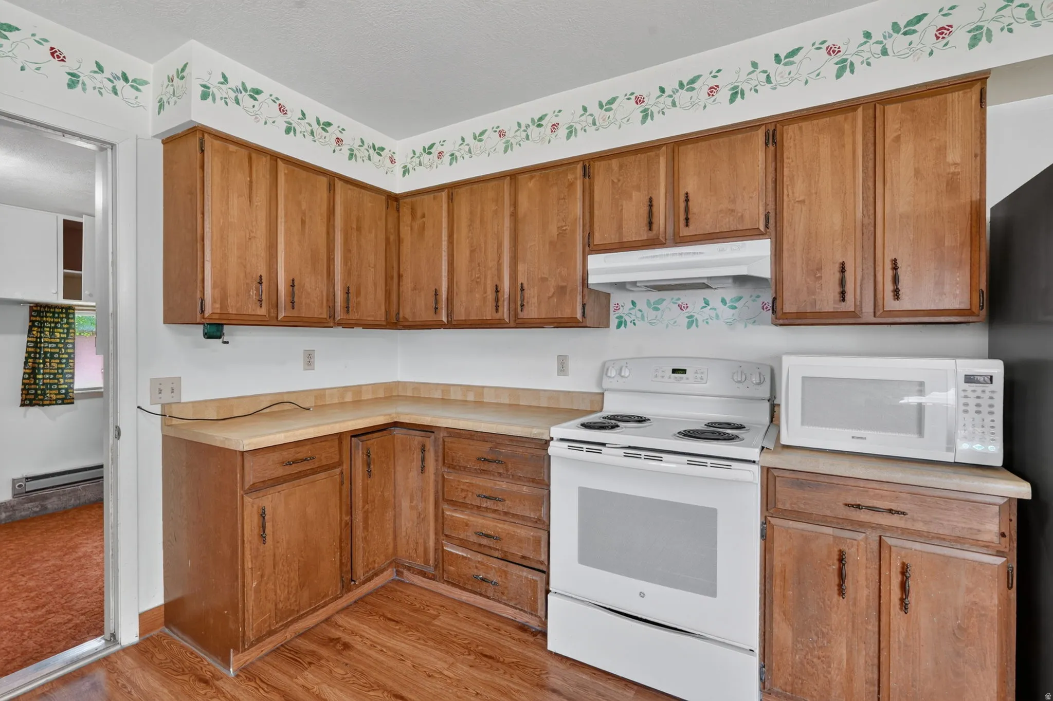Corner kitchen featuring wood-finish cabinetry, a freestanding range, a microwave, wood-finish flooring, and light-toned countertops