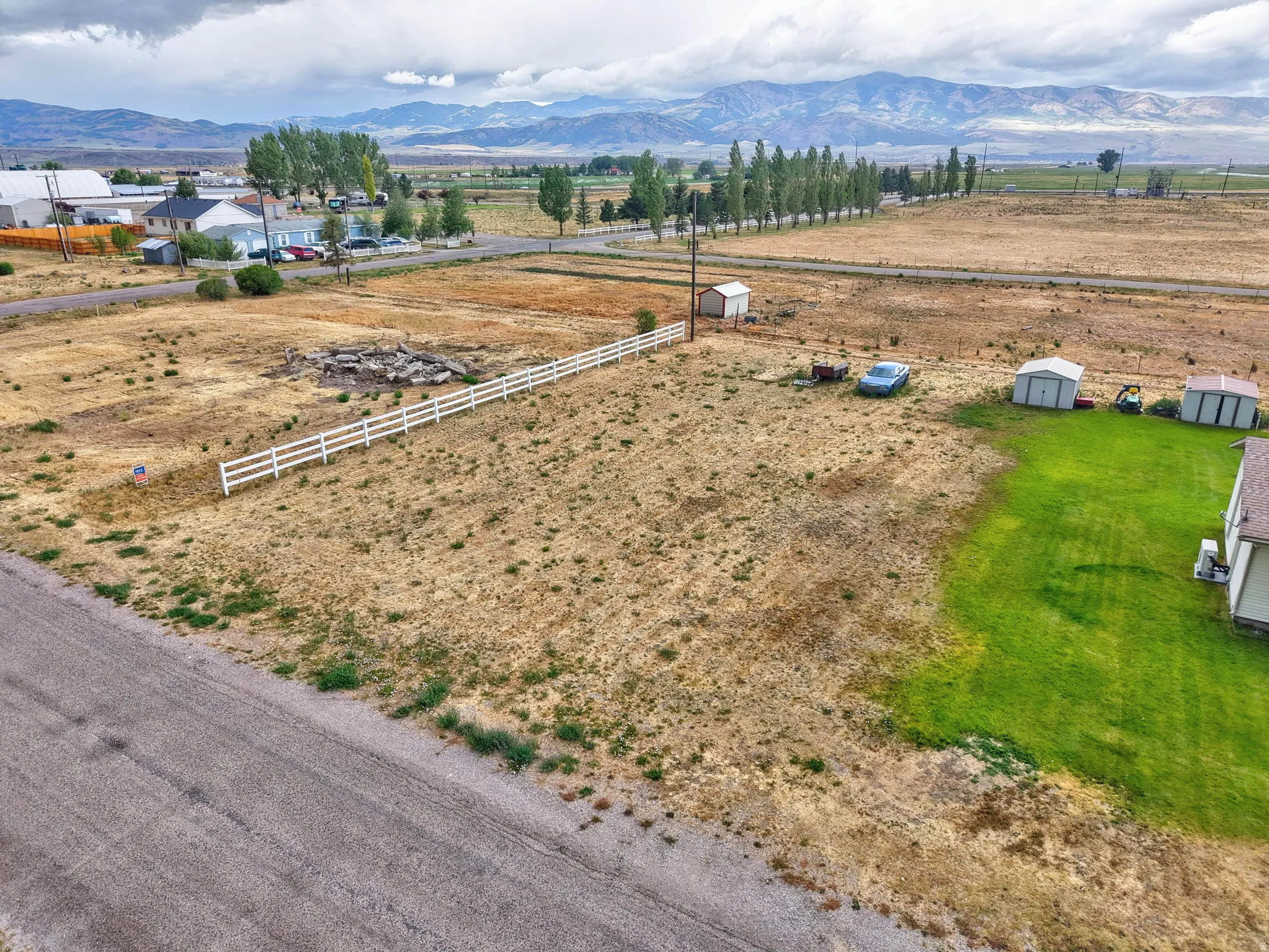Expansive lot with a white three-rail fence, distant mountain range, and partial green lawn