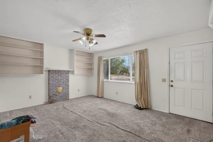 Brick fireplace with a mantel, flanking built-in shelving, ceiling fan with illumination, and a paneled entry door