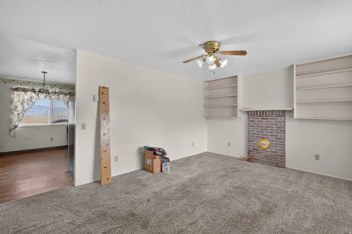 Carpeted living area with a brick fireplace, built-in shelving, and a ceiling fan