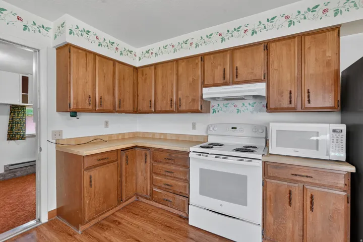 Corner kitchen featuring wood-finish cabinetry, a freestanding range, a microwave, wood-finish flooring, and light-toned countertops