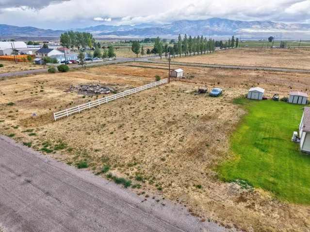 Expansive lot with a white three-rail fence, distant mountain range, and partial green lawn