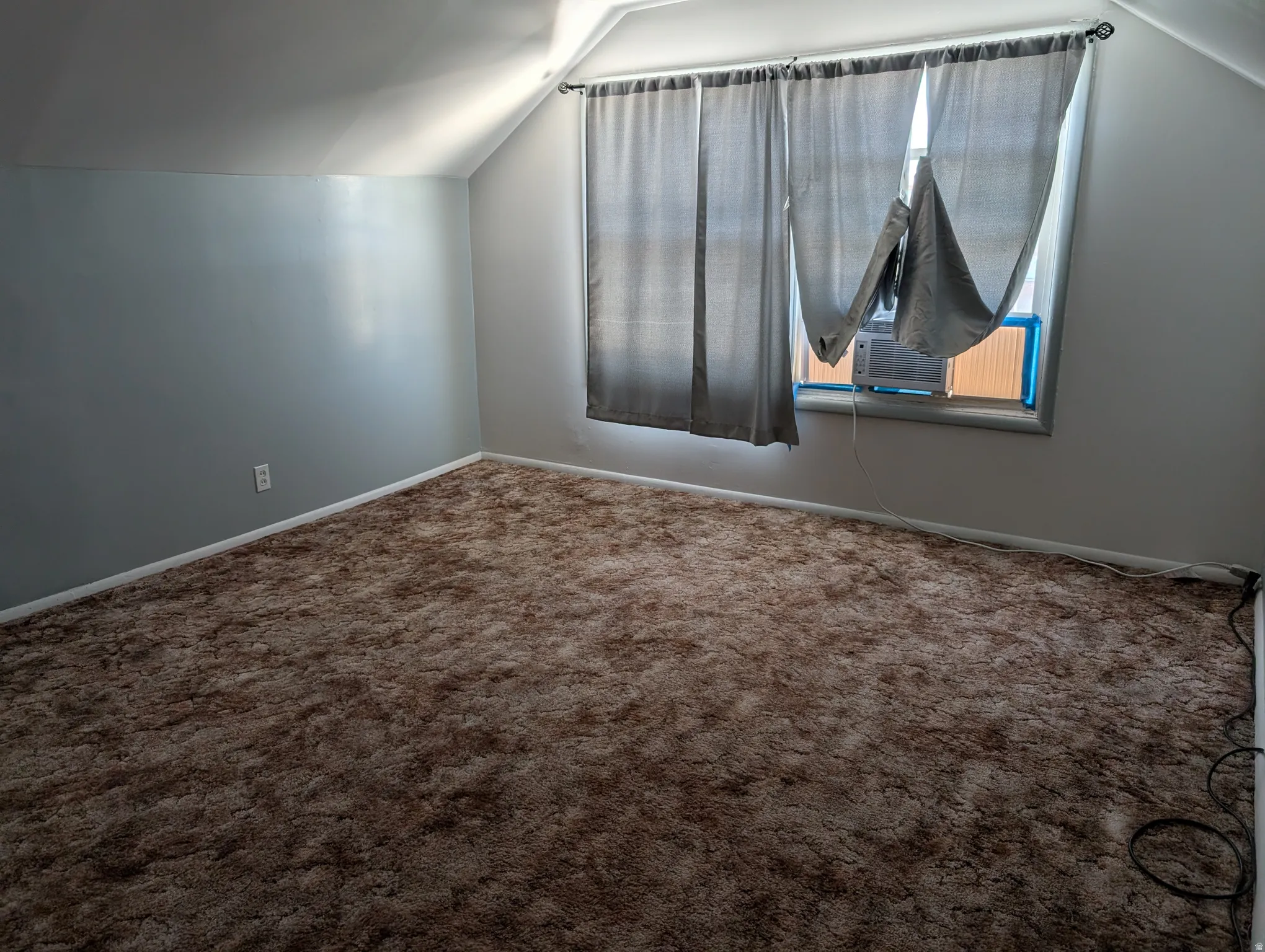 Sloped ceiling architecture with recessed window, wall-mounted air conditioning unit, and plush wall-to-wall carpeting