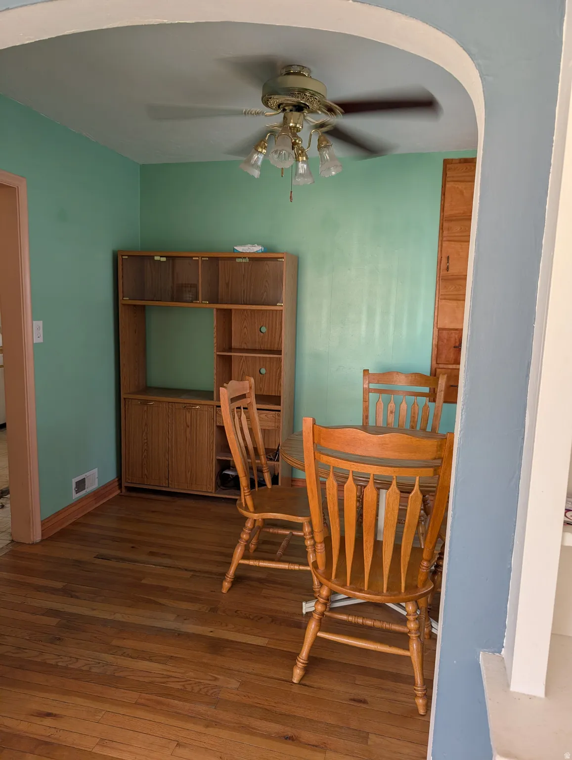 Hardwood flooring, arched doorway, ceiling fan with light fixture, built-in cabinetry, and light green wall finish