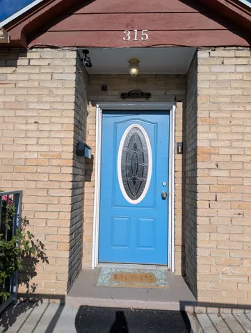 Brick exterior with a vibrant blue entry door, featuring an oval decorative glass insert, a black mailbox, and an overhead porch light