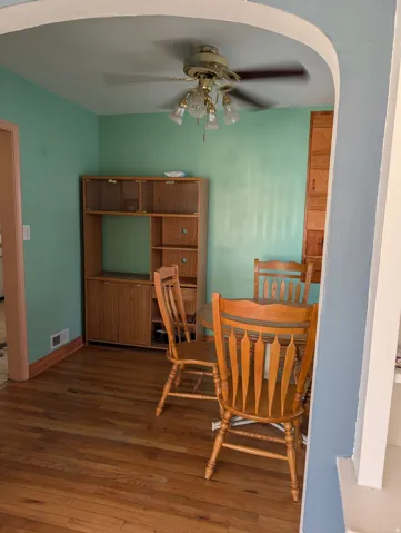 Hardwood flooring, arched doorway, ceiling fan with light fixture, built-in cabinetry, and light green wall finish