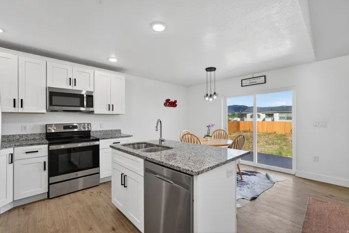 Modern kitchen featuring white cabinetry with brushed nickel hardware, stainless steel appliances including a gas range and microwave, granite countertops, and a large center island with seating