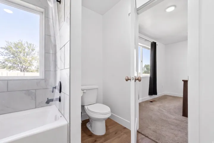 Bathroom featuring a white toilet, wood-finish flooring, a white bathtub, and tile surround with a window