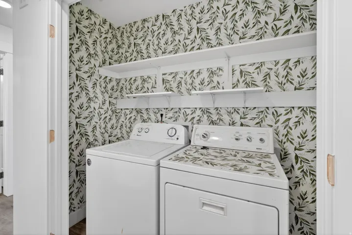 Utility area with botanical-patterned wallpaper, white appliances, and built-in white shelving