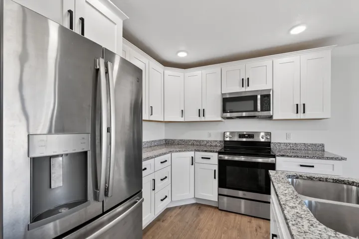 Modern kitchen featuring white cabinetry with black hardware, stainless steel appliances including a French door refrigerator with ice and water dispenser, electric range, and microwave, granite-style countertops, a subway tile backsplash, recessed ceilin