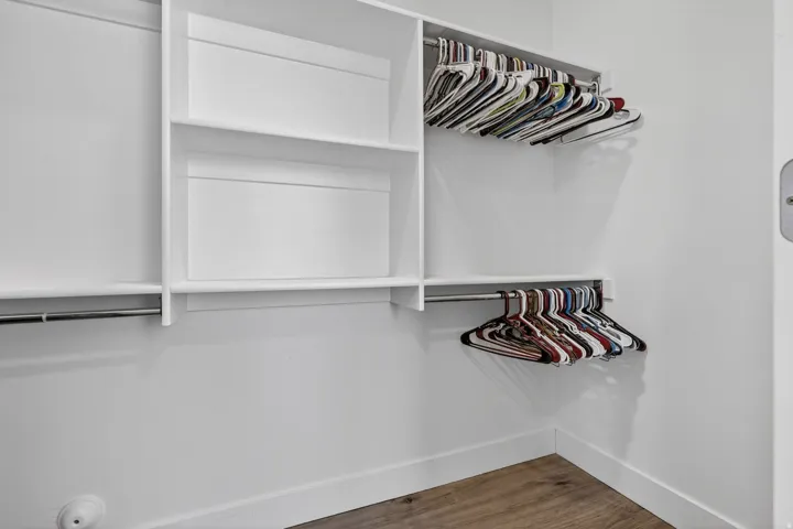 Integrated closet system featuring multiple shelves, two clothing rods, and wood-finish flooring