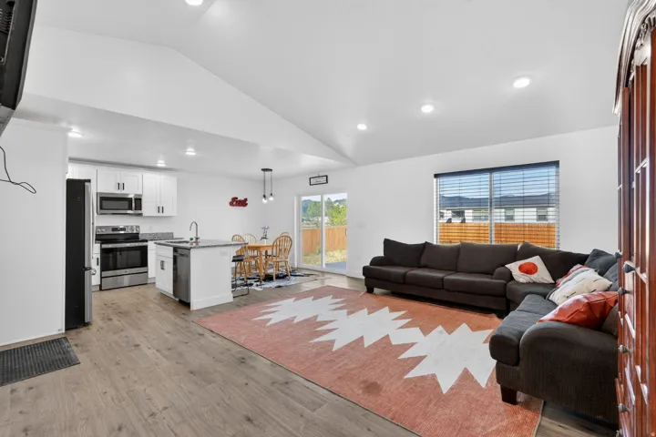 Vaulted ceilings, wood-finish flooring, white cabinetry, stainless steel appliances, and a sliding glass door