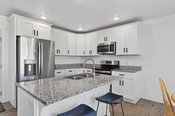 Modern kitchen featuring white cabinetry with brushed nickel hardware, granite-finish countertops, a large center island with breakfast seating, stainless steel appliances including a side-by-side refrigerator and built-in microwave, recessed lighting, an