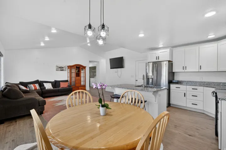 Vaulted ceilings with recessed lighting, wood-finish flooring, white cabinetry with black hardware, stainless steel refrigerator, and granite countertops