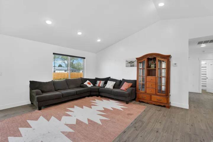 Vaulted ceiling with recessed lighting, wood-finish flooring, and a large window with blinds