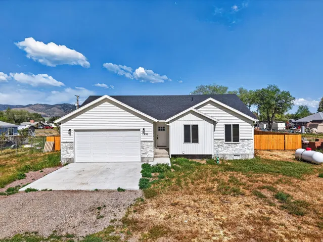 Modern ranch-style home featuring a clean white exterior with stone accents, two-car garage with white overhead door, gabled roofline with dark asphalt shingles, and a newly poured concrete driveway